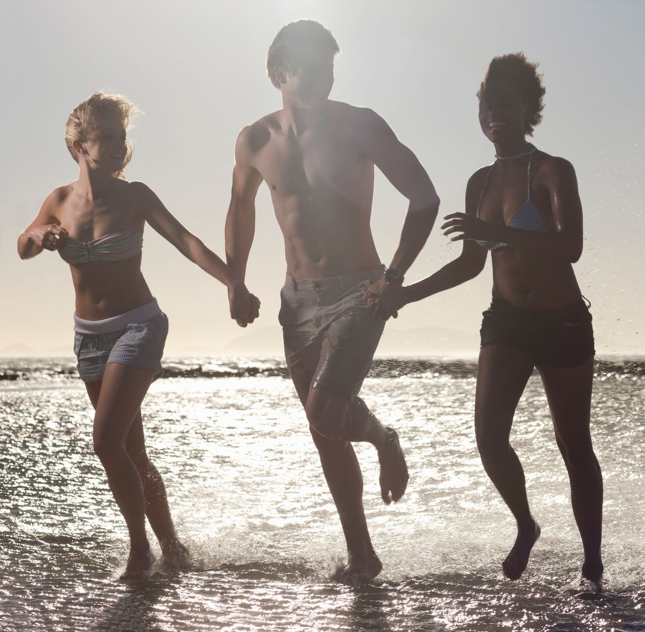Trois personnes se tiennent la main en courant dans les eaux peu profondes de l'océan au coucher du soleil.