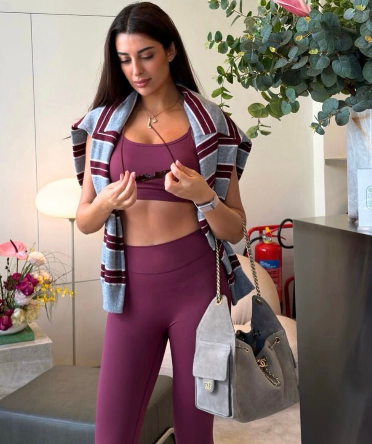 Une personne portant un soutien-gorge de sport et des écouteurs sans fil regarde sa montre connectée, assise dans une salle de sport lumineuse.