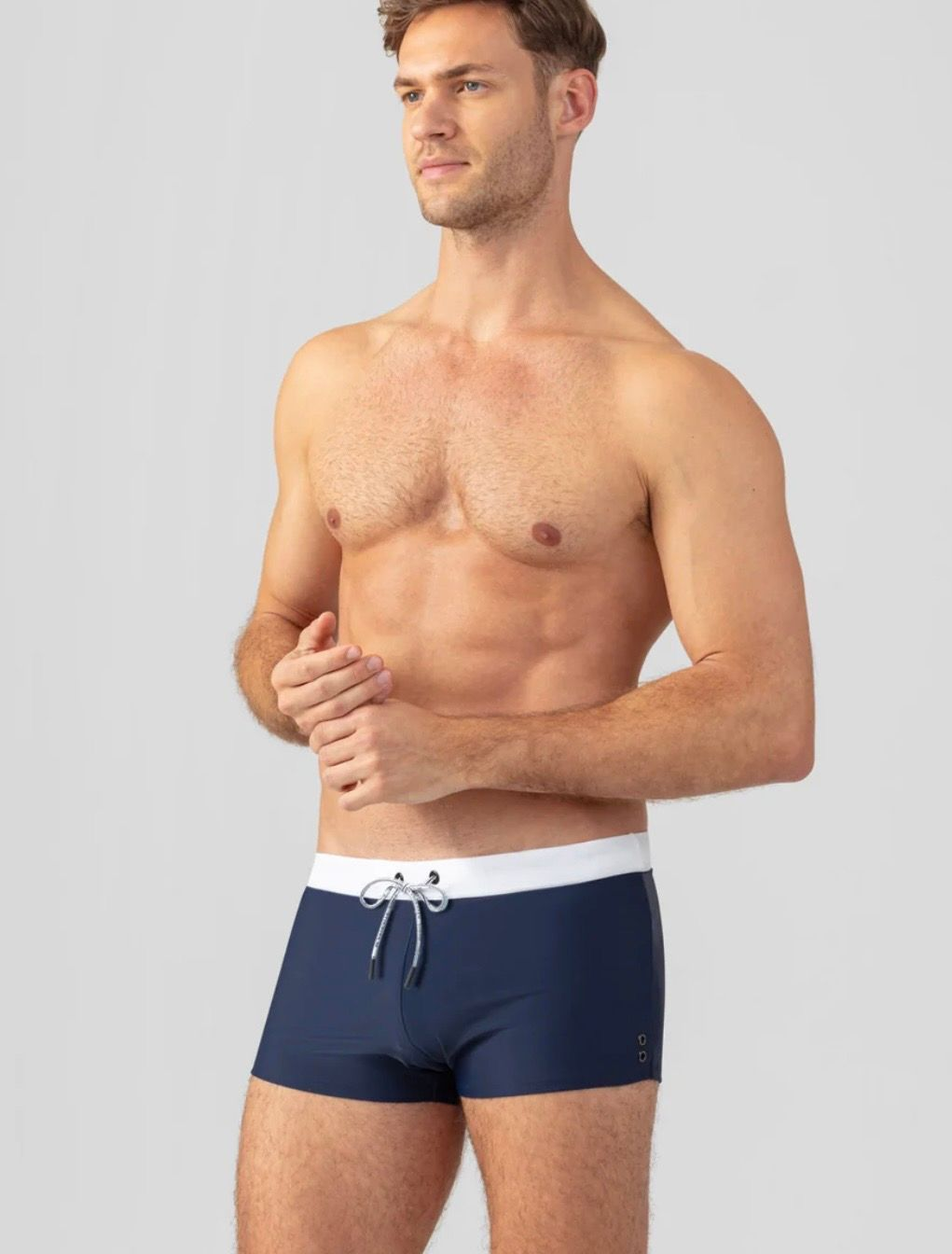 Une personne à la carrure musclée sourit, debout dans une piscine éclatant jusqu'à la taille, sous un ciel dégagé.