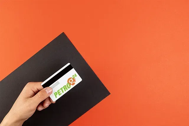 Mano sosteniendo una tarjeta de gasolinera Petro 24, rayas blancas y negras, fondo naranja.