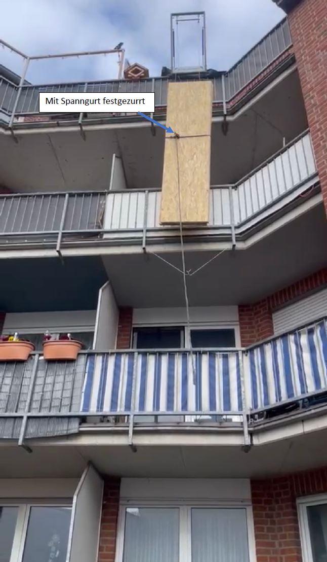 Eine hohe Holzplatte wird zwischen den Balkonen eines Backsteinwohnhauses hochgezogen.