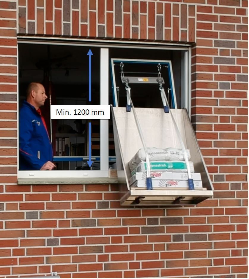 Mann benutzt einen Aufzug vor einem Fenster, um Kisten zu bewegen. Rotes Backsteingebäude.