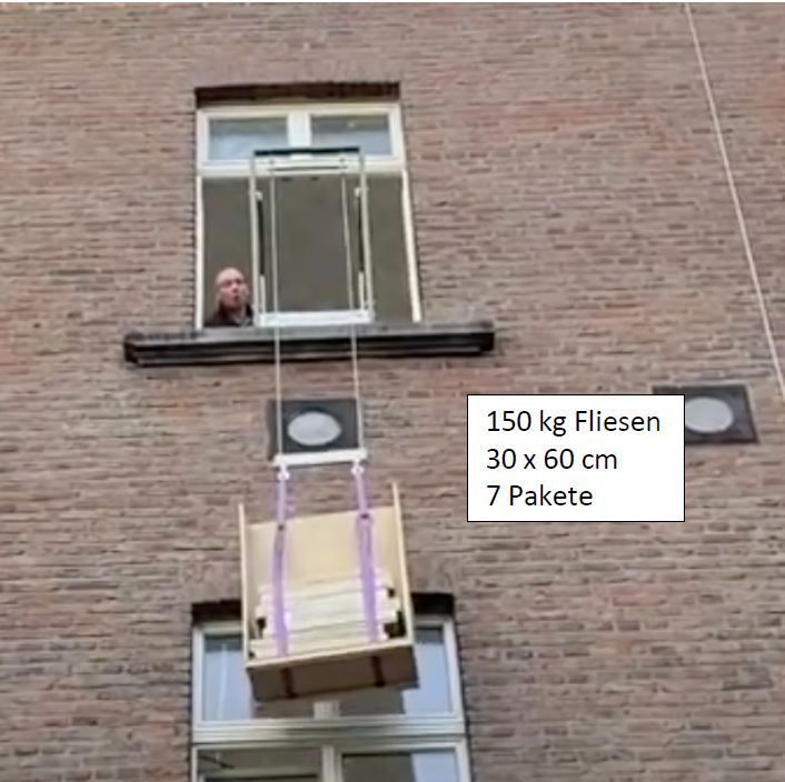 Ein Mann in einem Fenster bedient einen Flaschenzug, der 150 kg Ziegel an der Seite eines Backsteingebäudes hochhebt.