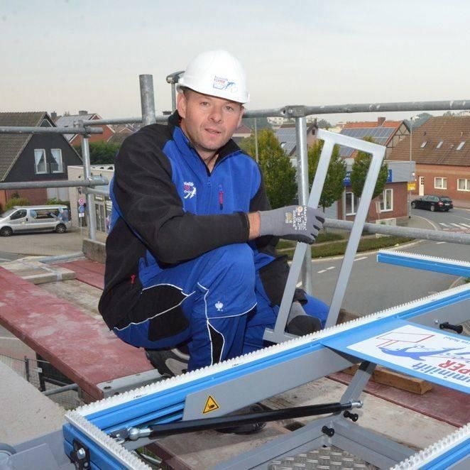Bauarbeiter in blauem Overall und Schutzhelm auf dem Dach, hält Metallrahmen.