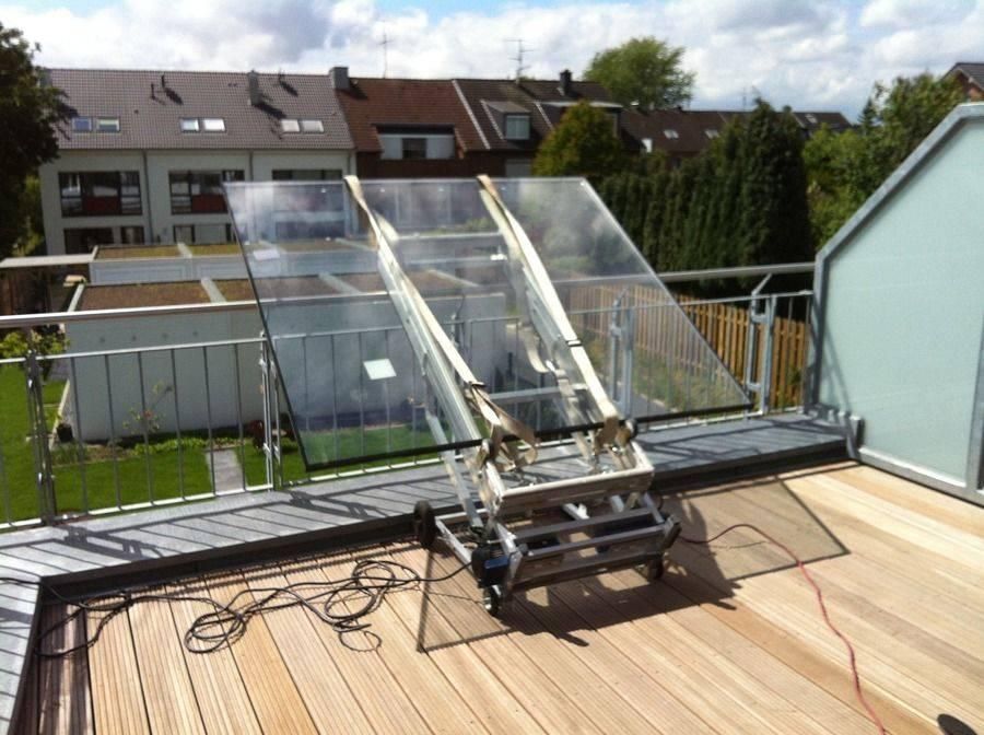 Solarpanel-Installation auf einem Deck mit Metallrahmen, Glasplatten und Stromkabeln. Holzdeck im Hintergrund.