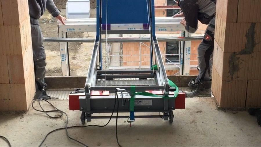 Zwei Bauarbeiter benutzen einen Aufzug, um ein Fenster in ein Gebäude einzubauen.