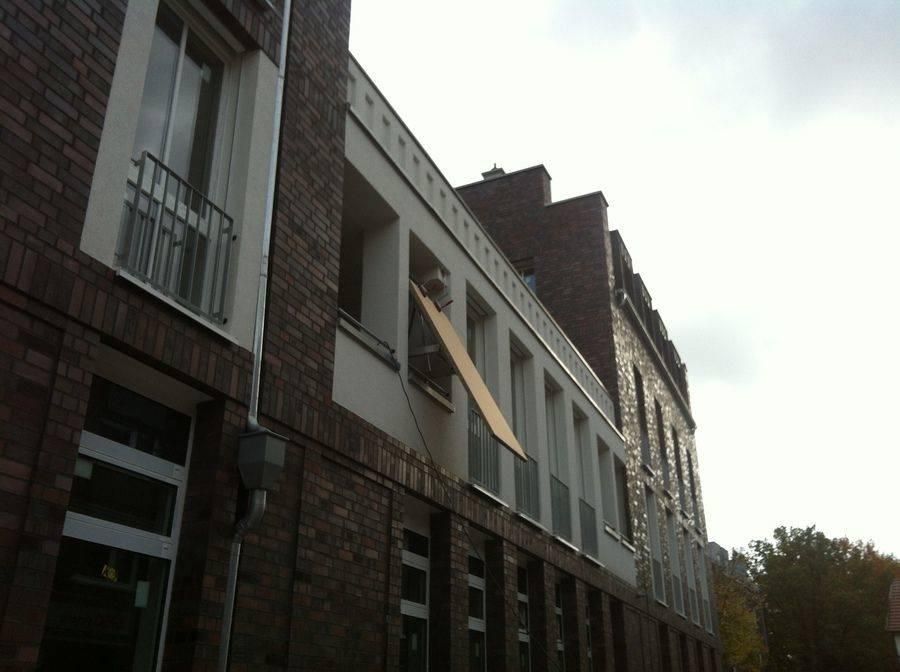 Backsteingebäude mit mehreren Stockwerken, Fenstern und Balkonen. Von einem Balkon hängt ein großes rechteckiges Paneel.