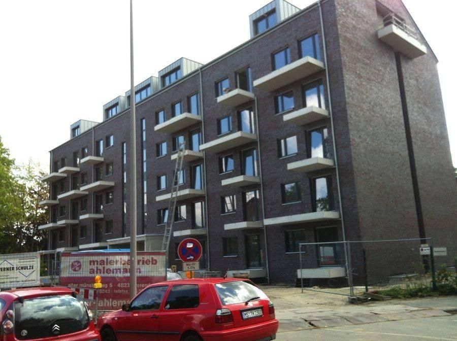 Mehrstöckiges Backsteinwohnhaus mit Balkonen, im Bau, rotes Auto davor.