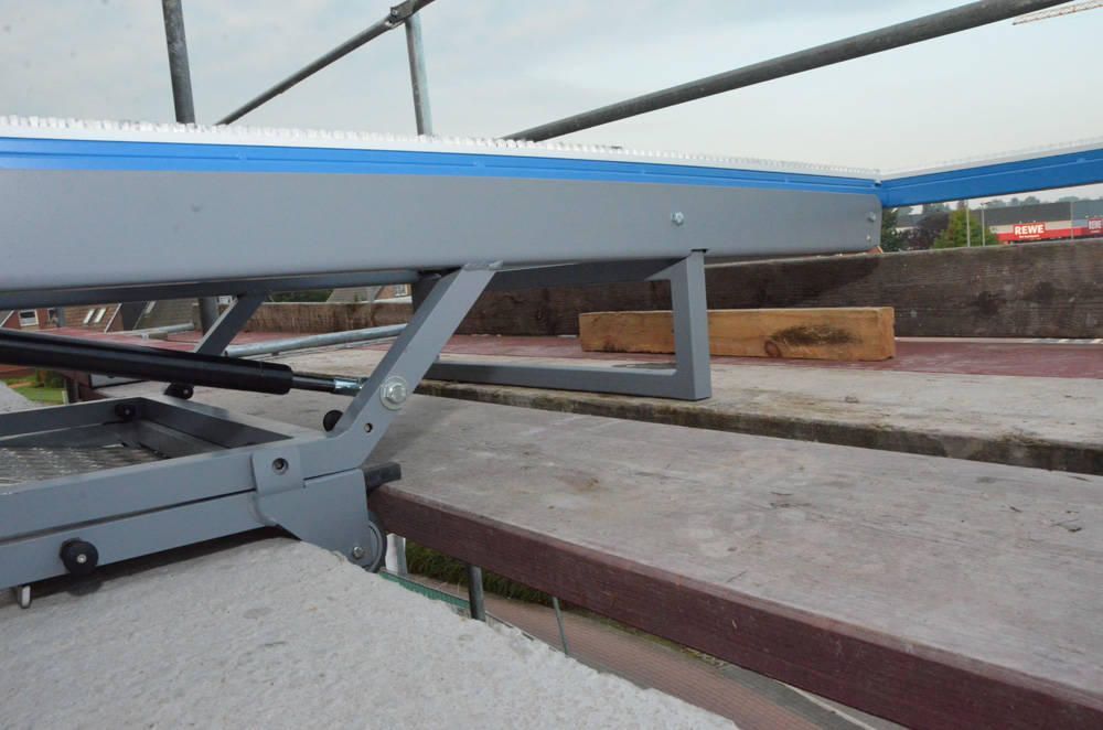 Eine graue Hebebühne mit blau-weißer Oberseite; auf einer Betonoberfläche sind Stützen und ein hydraulischer Aufzug sichtbar.