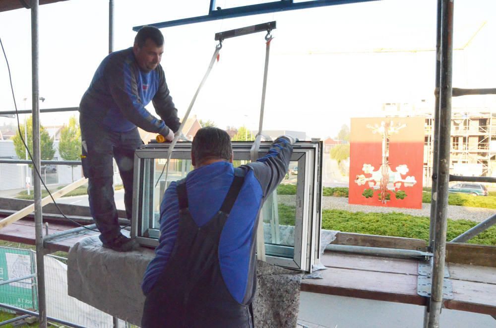 Zwei Arbeiter installieren ein Fenster und heben es mithilfe von Seilen von einer Plattform.