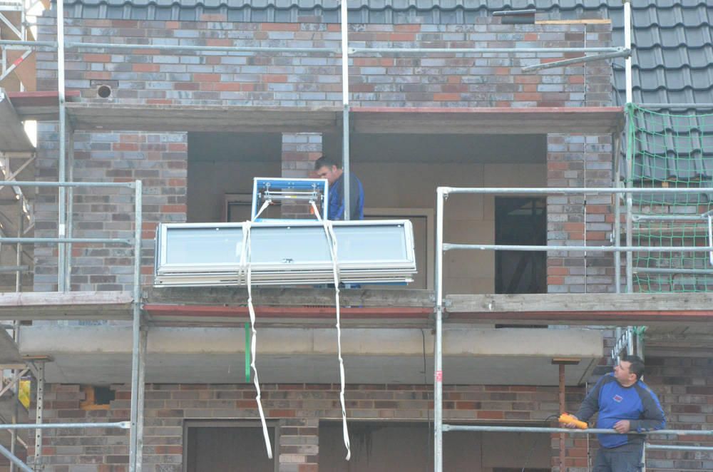 Zwei Bauarbeiter installieren mithilfe eines Gerüsts ein Fenster in einem Gebäude.