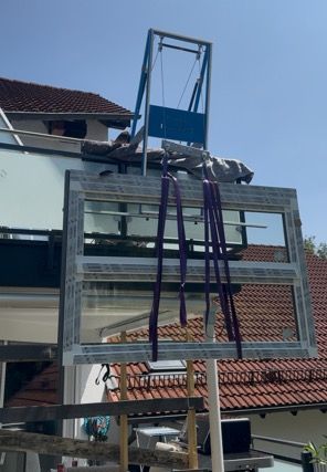 Vor einem Haus mit rotem Ziegeldach wird ein Fenster mit einem Hebezeug angehoben.