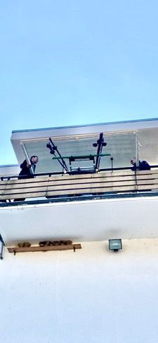 Menschen in der Nähe eines Balkons mit einem Fahrradständer, darüber heller Himmel.