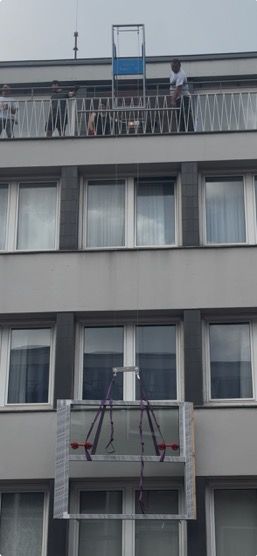Gebäudefassade mit einer abgehängten Fensterputzplattform und einer Person auf dem Balkon.