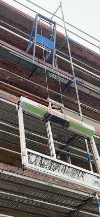 Ein Fenster wird mit einem Hebezeug auf einem Baugerüst angehoben.