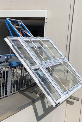 Ein großes Fenster wird von einem blauen Kran vor einem Gebäude angehoben.