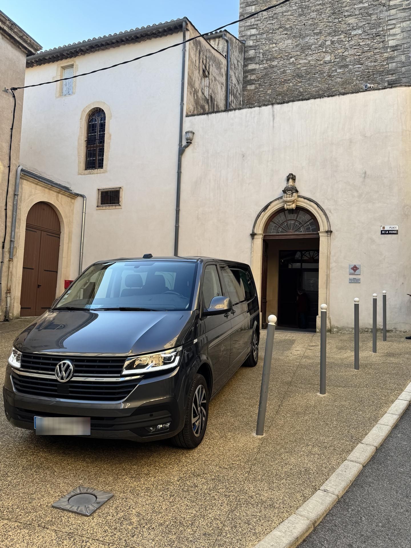 Une camionnette noire garée à côté de l'entrée d'une petite église blanche dans une rue pavée