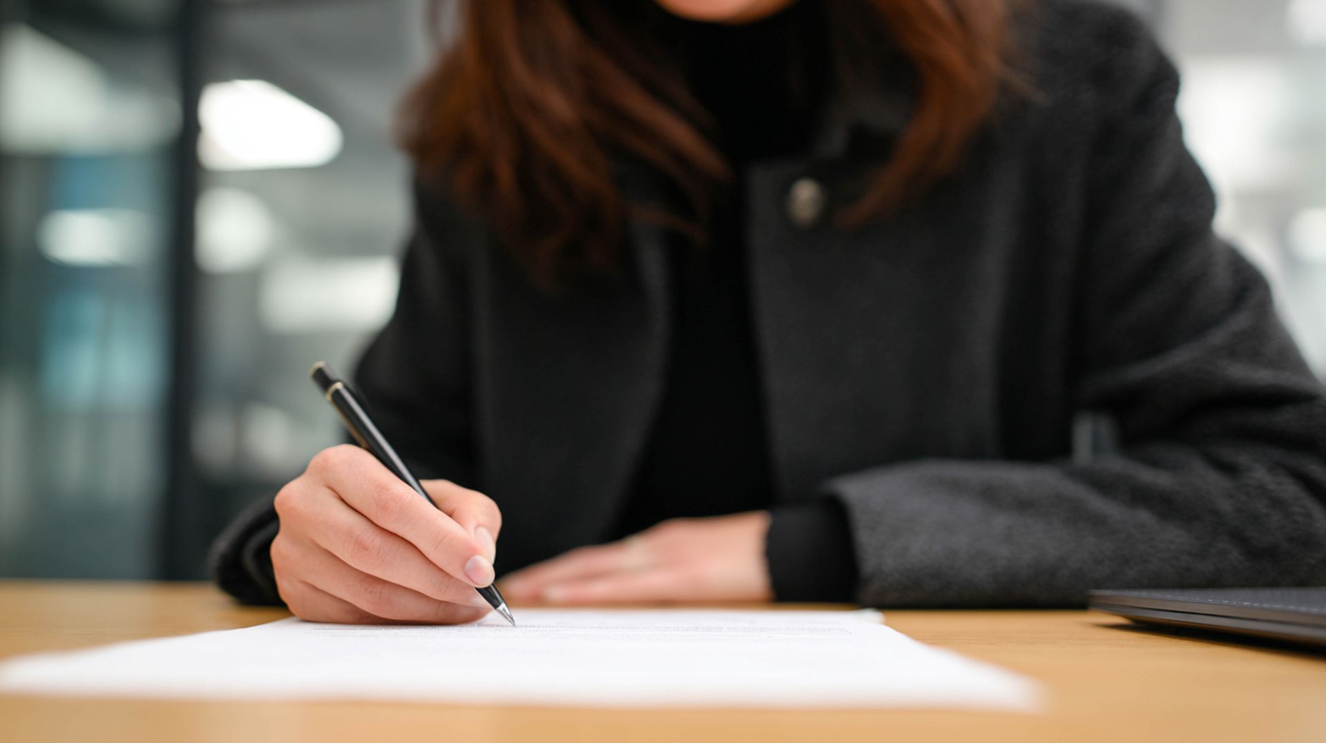 Une personne écrivant au stylo sur du papier à un bureau dans un environnement de bureau