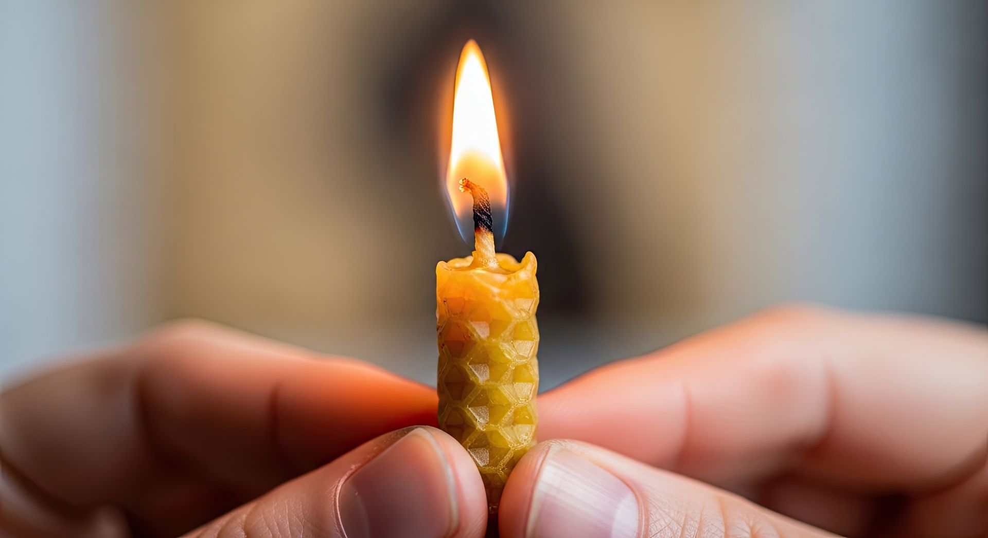 Une bougie jaune allumée, tenue entre deux doigts, avec une petite flamme sur un fond flou.