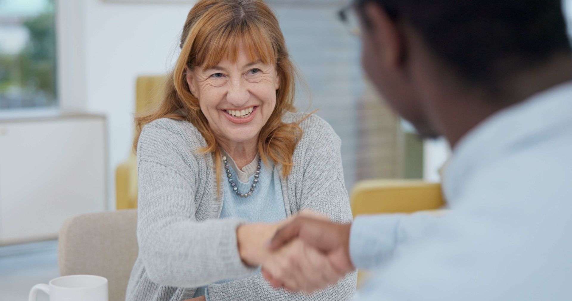 Dans un bureau lumineux, deux personnes se serrent la main par-dessus une table, l'une d'elles souriant chaleureusement.