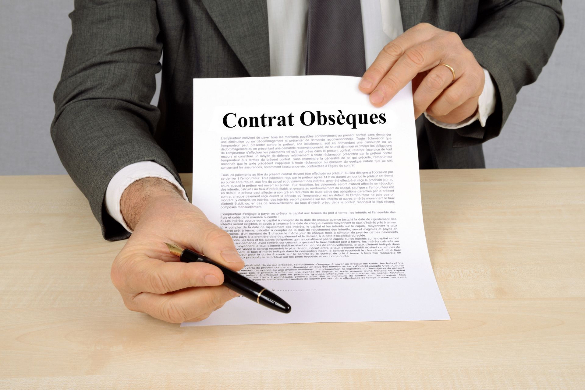 Une personne en costume gris signe un document intitulé Contrat Obsèques à un bureau