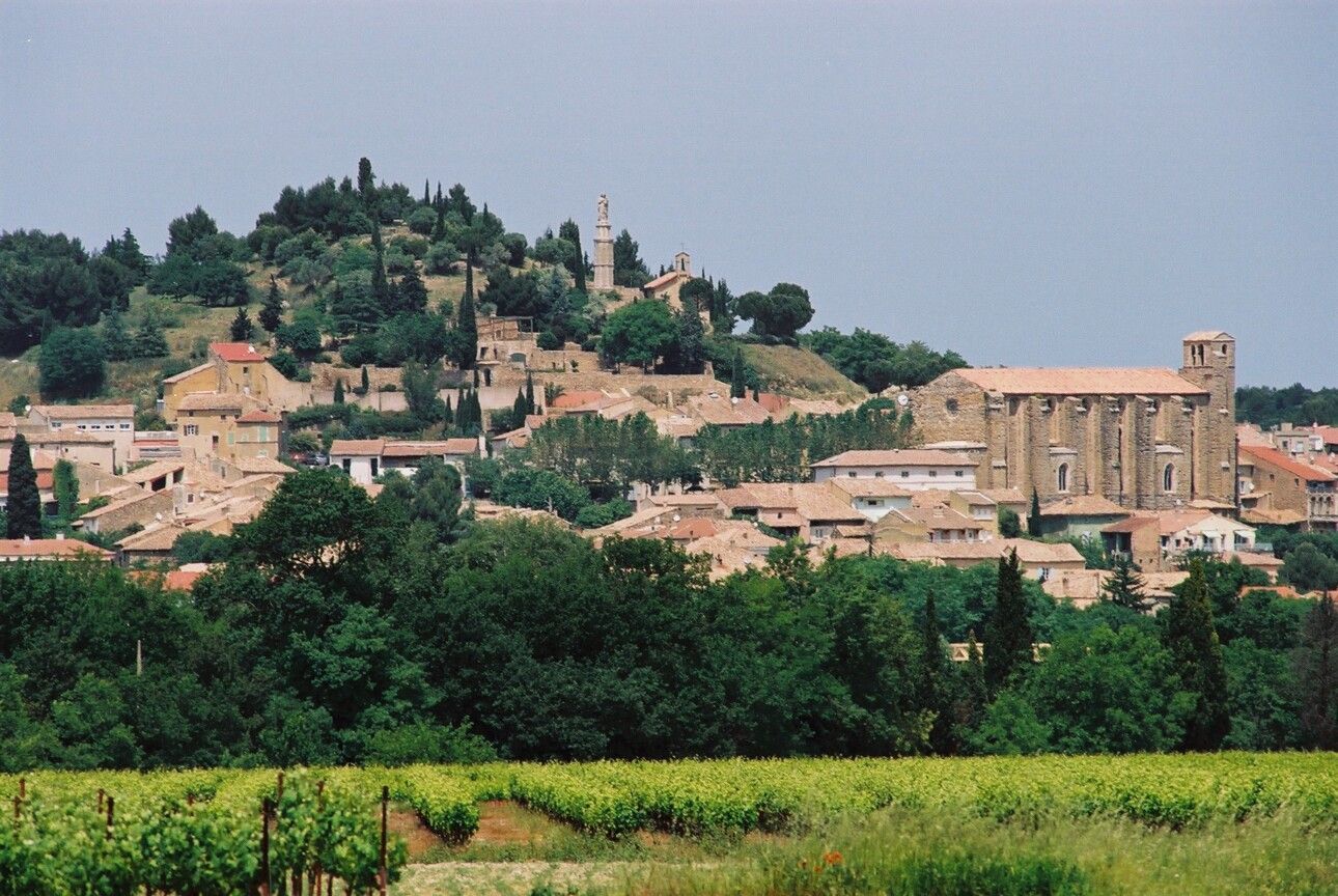 Village perché sur une colline, avec des bâtiments en pierre et des clochers d'église dominant des champs verdoyants sous un ciel brumeux