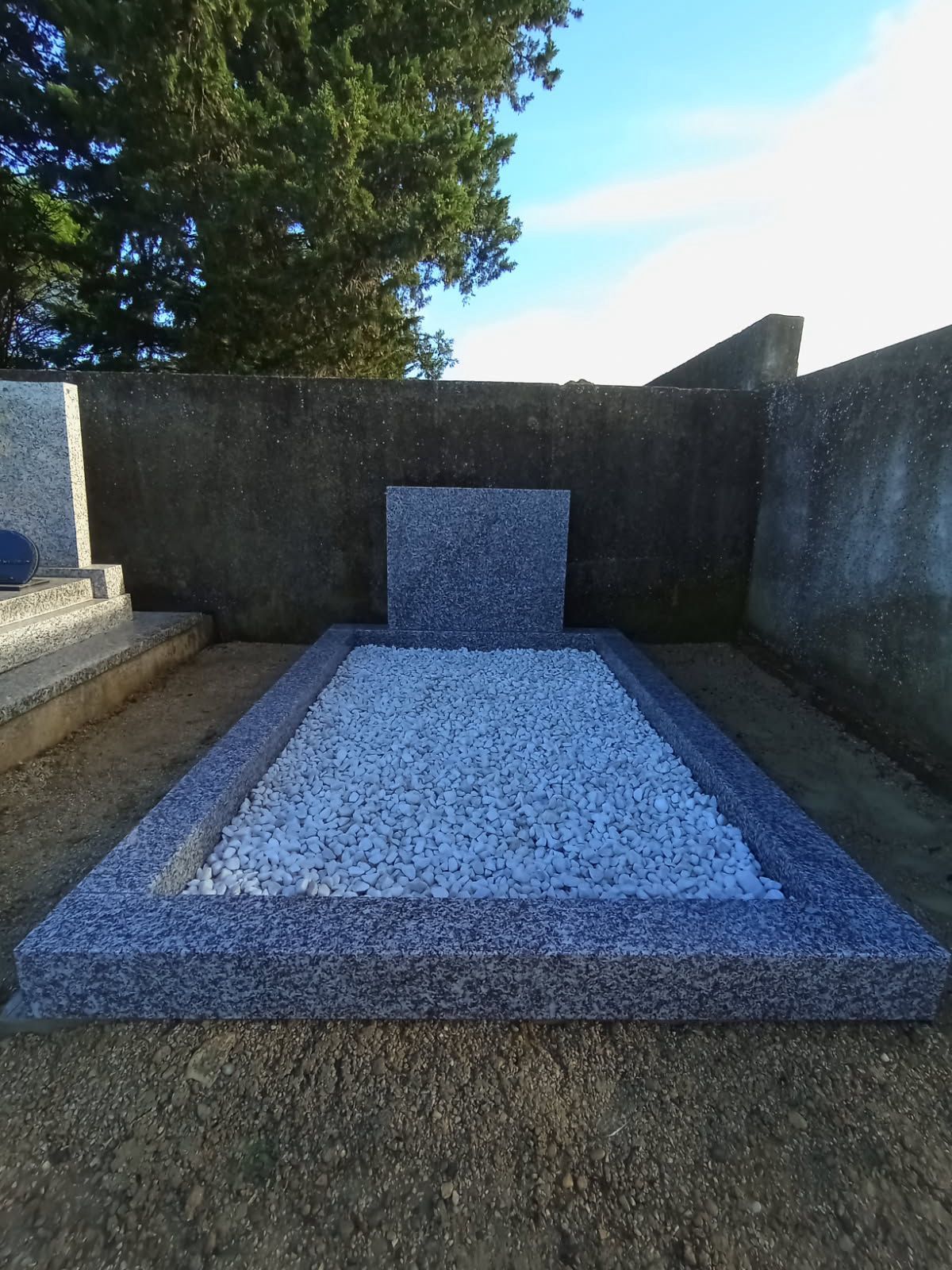 Monument commémoratif extérieur en pierre avec une bordure bleu-gris et du gravier blanc dans un jardin clos