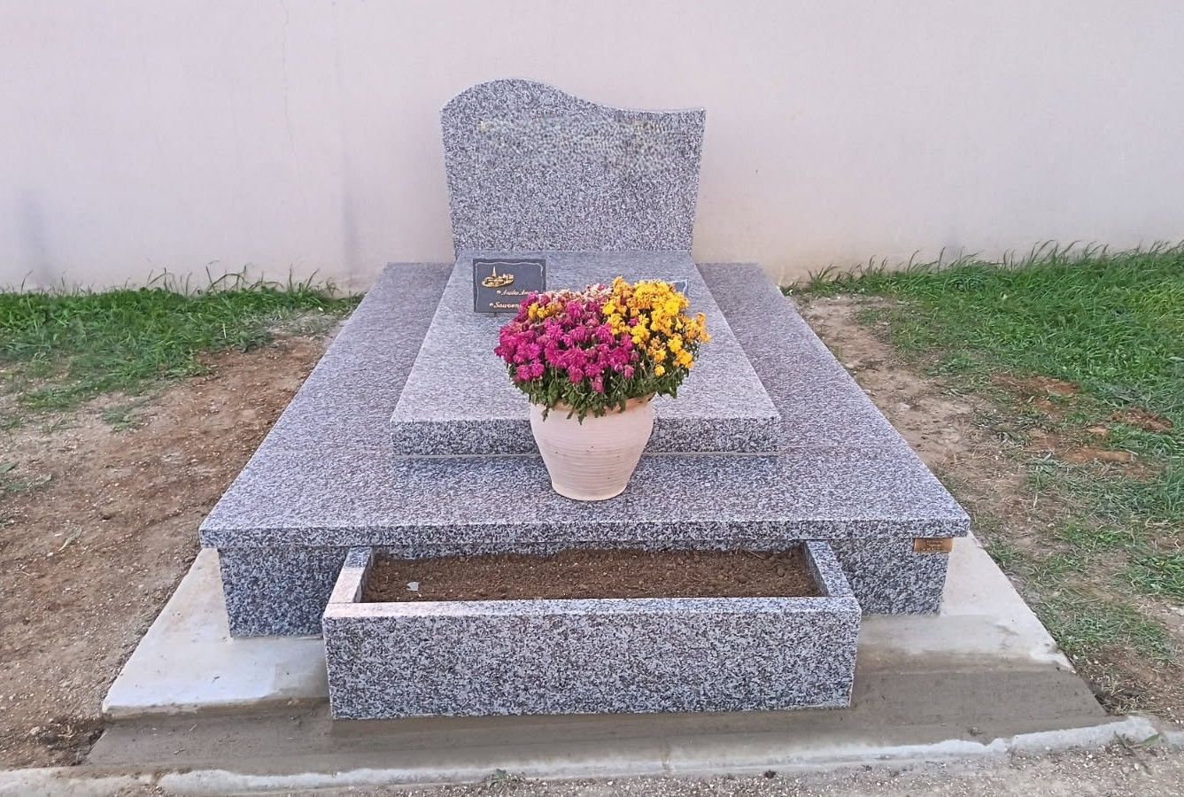 Une personne nettoie une pierre tombale blanche gravée dans un cimetière bordé d'arbres