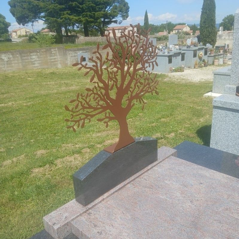 Pierre tombale en métal en forme d'arbre sur une parcelle de cimetière avec de l'herbe et d'autres pierres tombales en arrière-plan