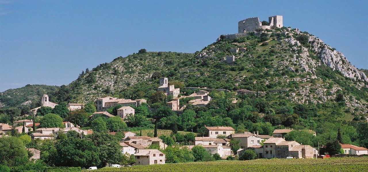Village à flanc de colline avec des maisons en pierre et un château au sommet d'une colline rocheuse et verdoyante sous un ciel clair