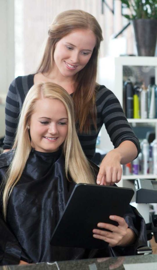 Una mujer se está cortando el pelo en la peluquería mientras mira una tableta.