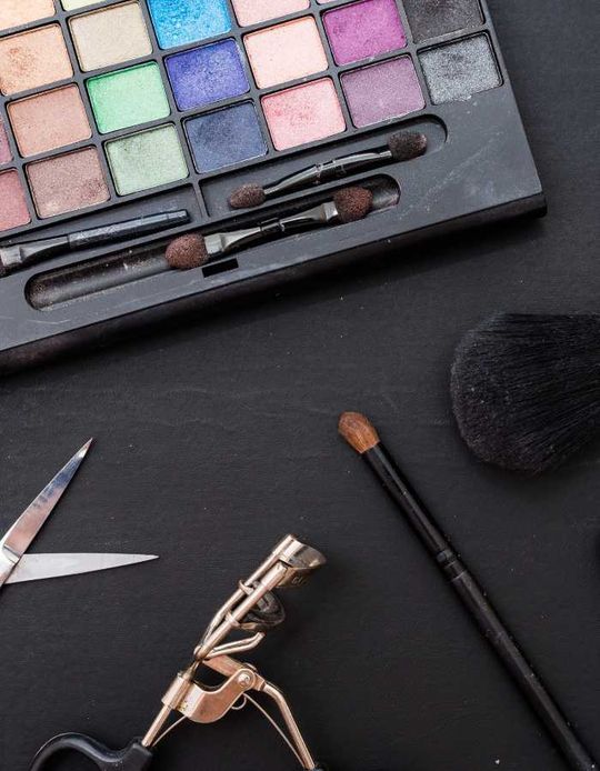 Una paleta de sombras de ojos, pinceles y tijeras sobre una mesa.
