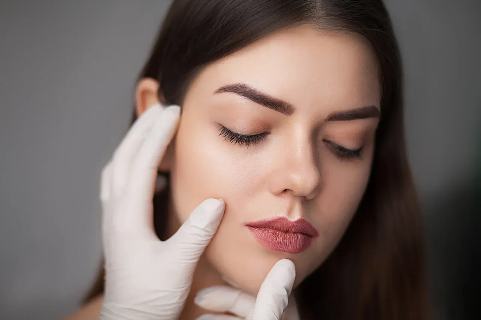 Mujer con los ojos cerrados y el rostro tocado por manos enguantadas.
