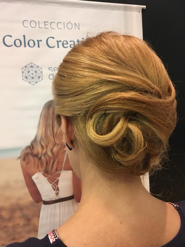 Mujer con peinado rubio recogido, delante de un cartel; vista posterior.