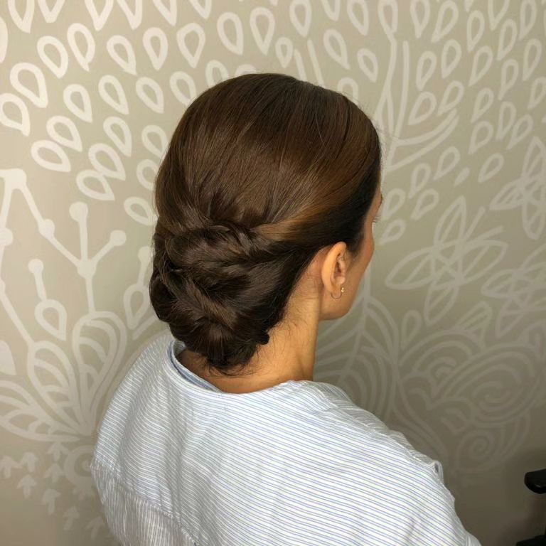 Mujer con cabello castaño peinado en un recogido con trenza, vistiendo una camisa de rayas azules y blancas.