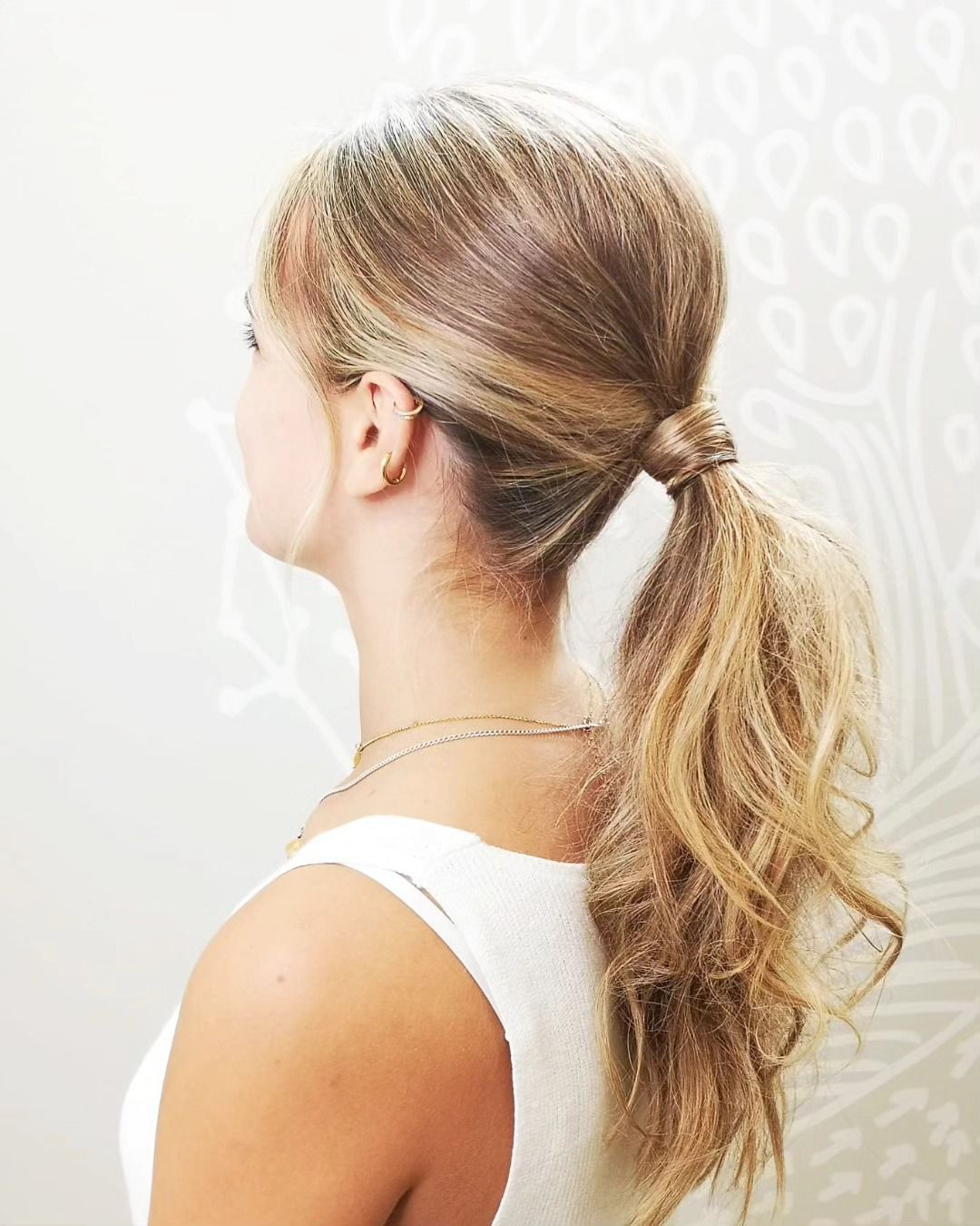 Cola de caballo rubia, vista lateral de una persona que lleva una camiseta blanca y un collar de oro.