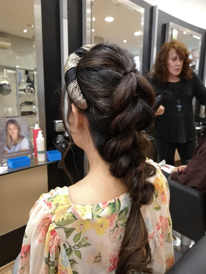 Mujer con cabello oscuro en el salón, peinado con una trenza y luciendo un top floral.