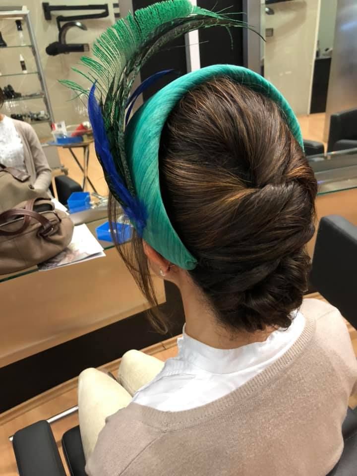 Mujer con cabello oscuro recogido en un moño, que lleva un tocado verde azulado y azul con plumas.