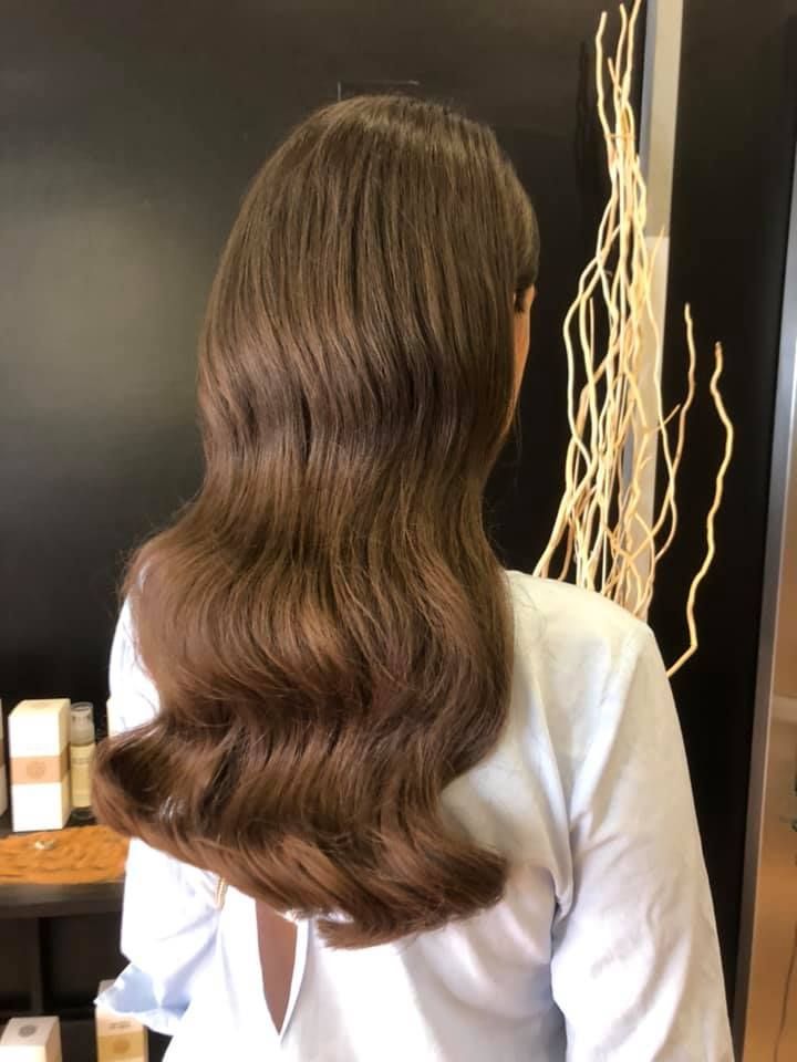 Mujer con cabello castaño ondulado. Camisa blanca. En una peluquería.