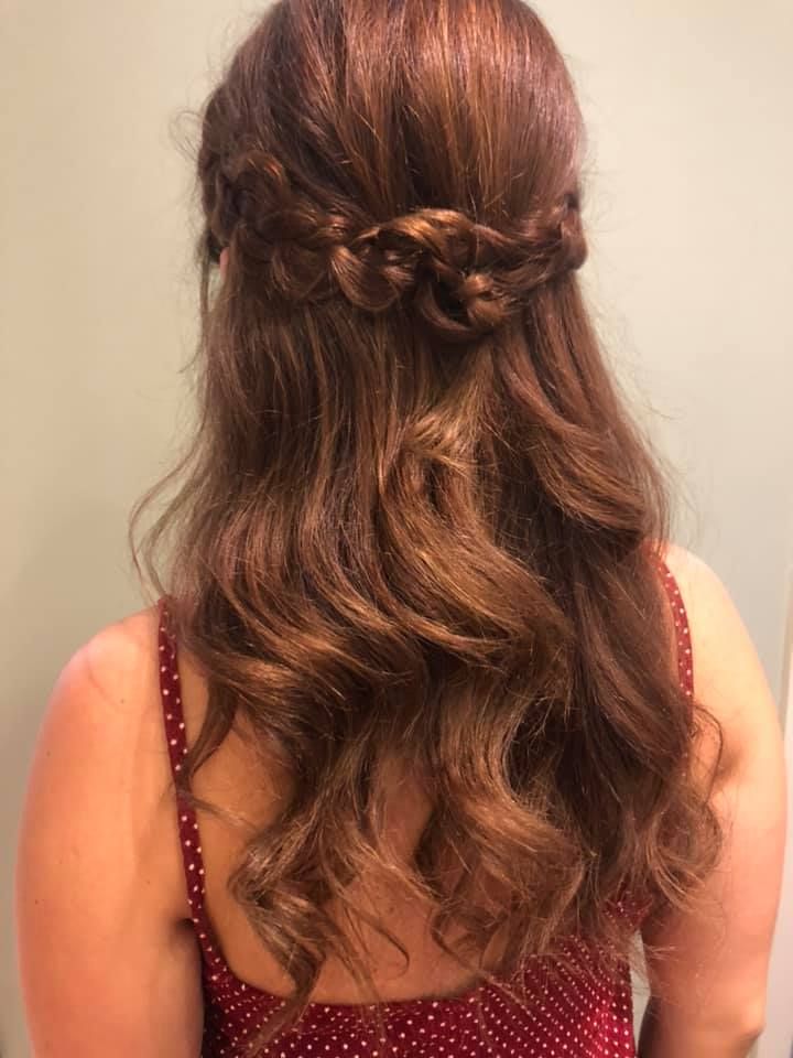 Mujer con cabello castaño, peinado con corona trenzada y ondas sueltas, vistiendo un top de lunares rojos.