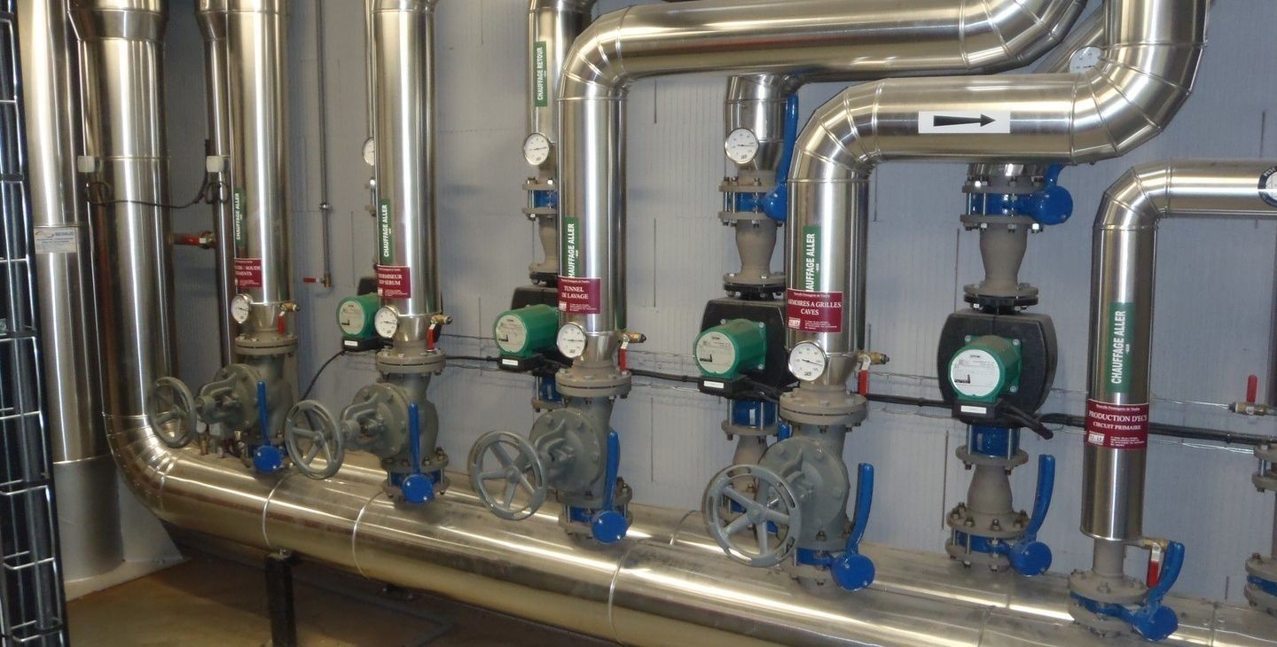 Tuyaux métalliques avec vannes et pompes, probablement pour le système de chauffage ou de climatisation d'un bâtiment.