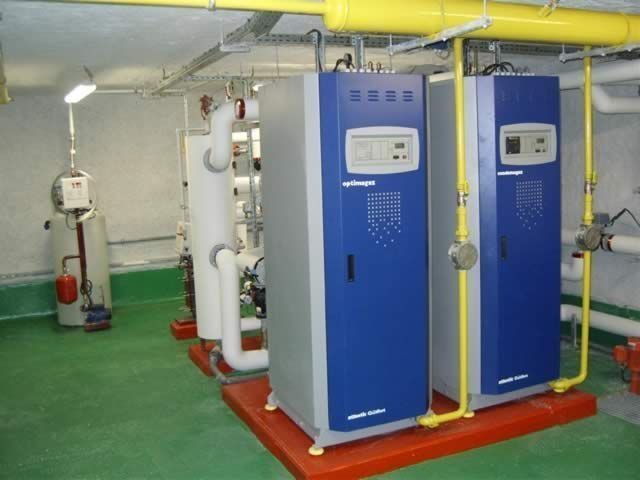 Deux chauffe-eau industriels bleus et gris sur un socle rouge dans une buanderie.