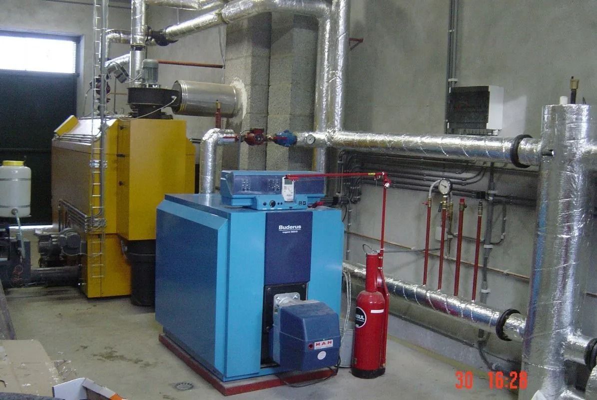 Chaufferie industrielle avec équipements bleus et jaunes, tuyaux et extincteur rouge.