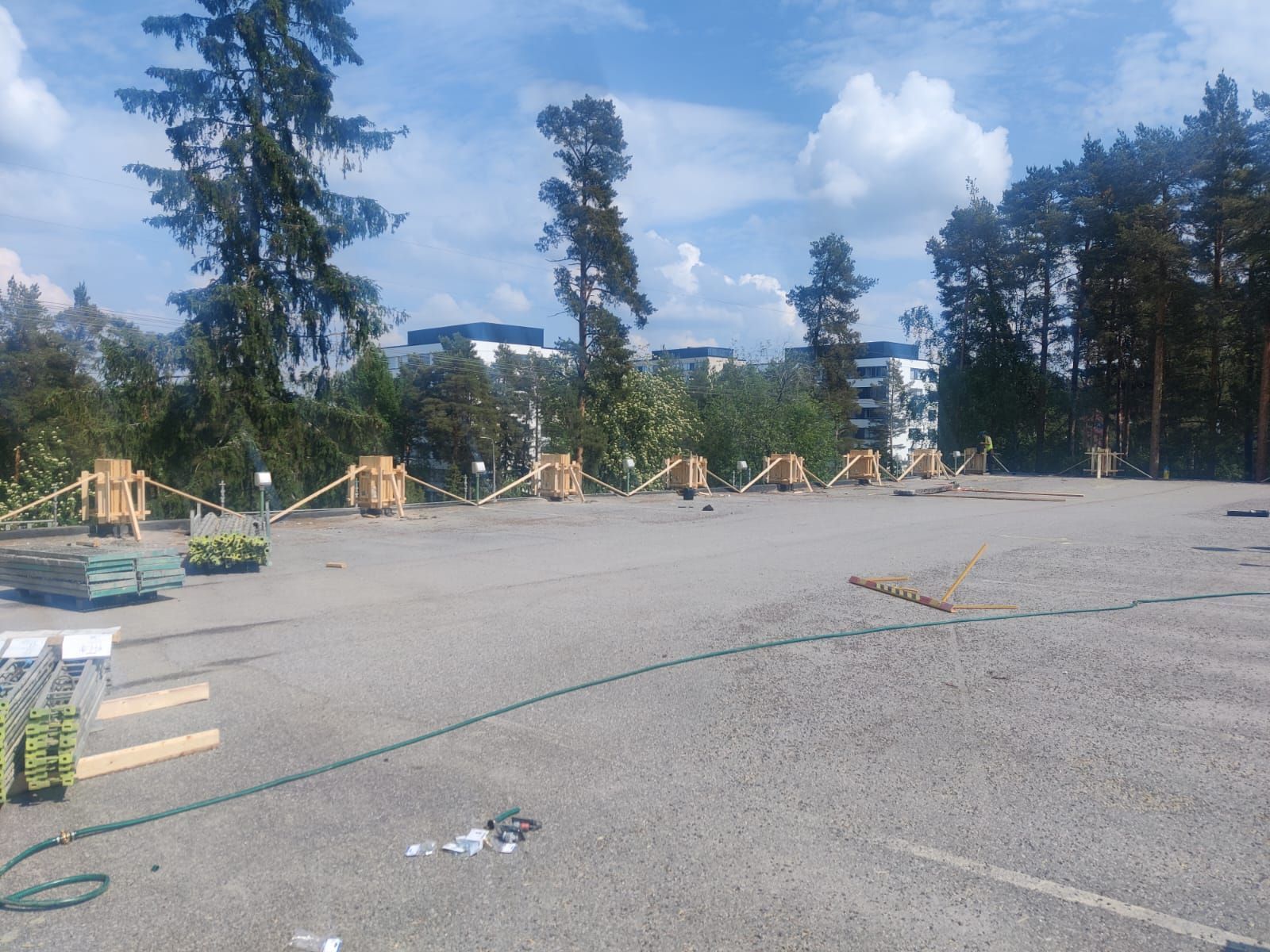 Köydellä erotettuja puisia laatikoita päällystetyllä pysäköintialueella, taustalla puita ja rakennuksia.