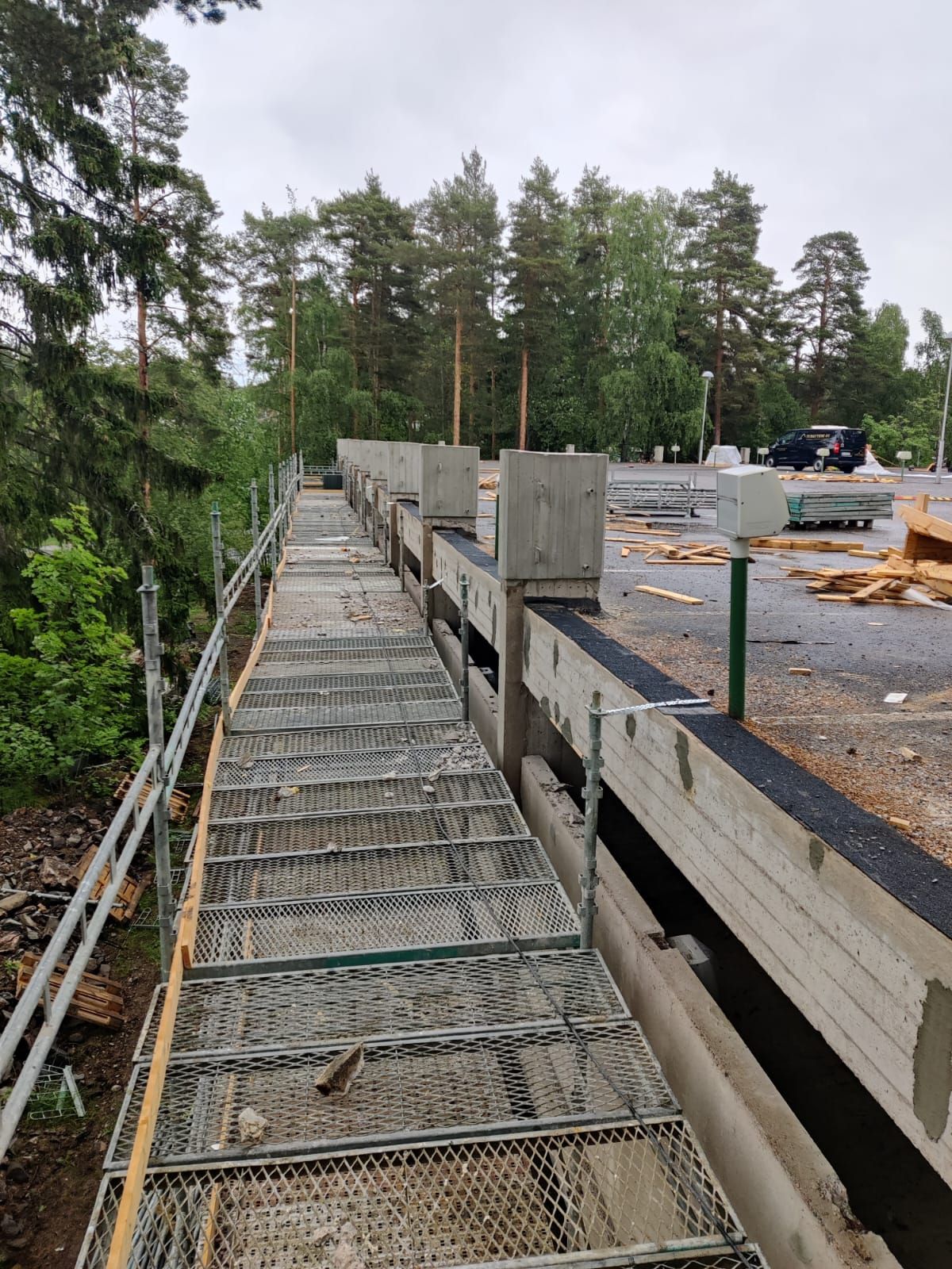 Rakennustelineiden kävelytie betonisen esteen ja rakennustyömaan vieressä, taustalla puita.