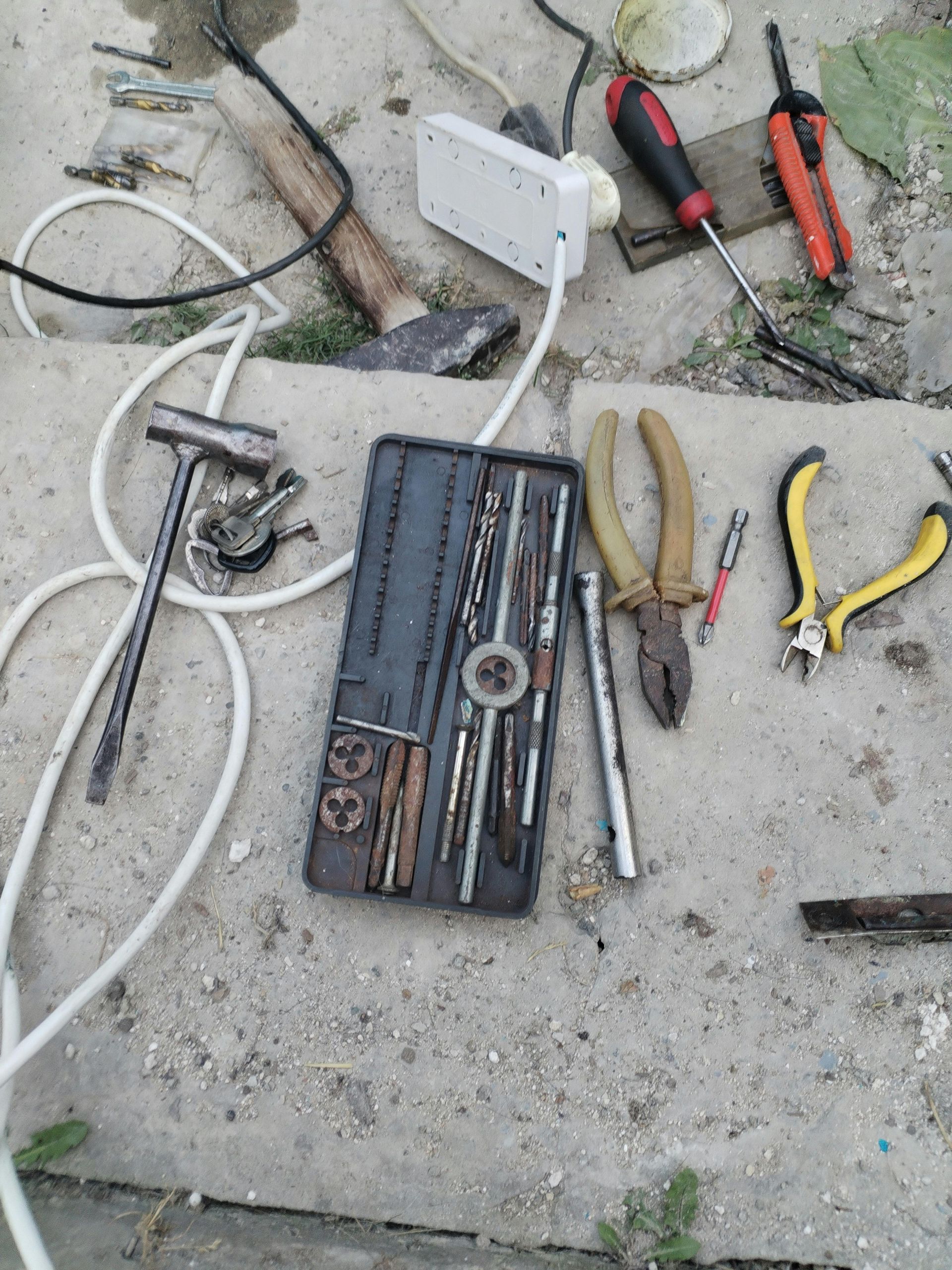 Sekalaisia ​​käsityökaluja, kuten pihdit, vasara ja kierretappi- ja muottisarja, on hajallaan betonipinnalla.