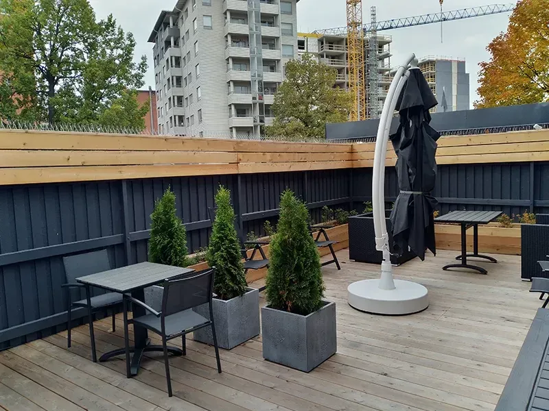 Ulkoterassi, jossa on puinen terassi, tummanharmaa näkösuoja-aita, pieniä ruukkukasveja ja pöytiä tuoleineen Turun kohteessa.