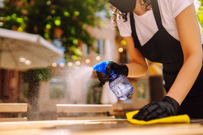 Una mujer que lleva una máscara está limpiando una mesa con una botella de spray.