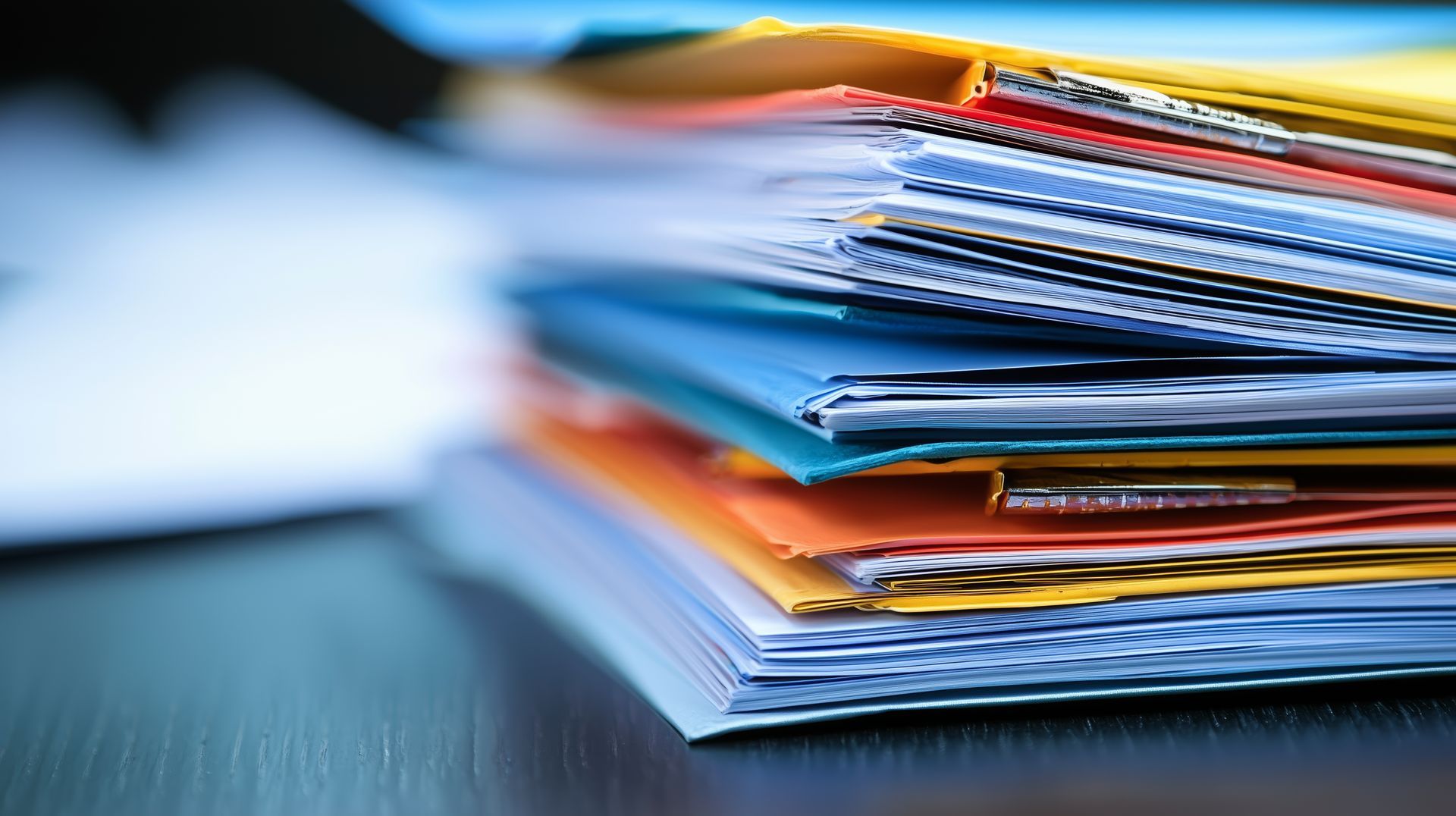 Pile de dossiers colorés sur un bureau, avec quelques papiers visibles.
