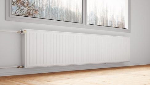 Un radiador blanco está junto a una ventana en una habitación vacía.